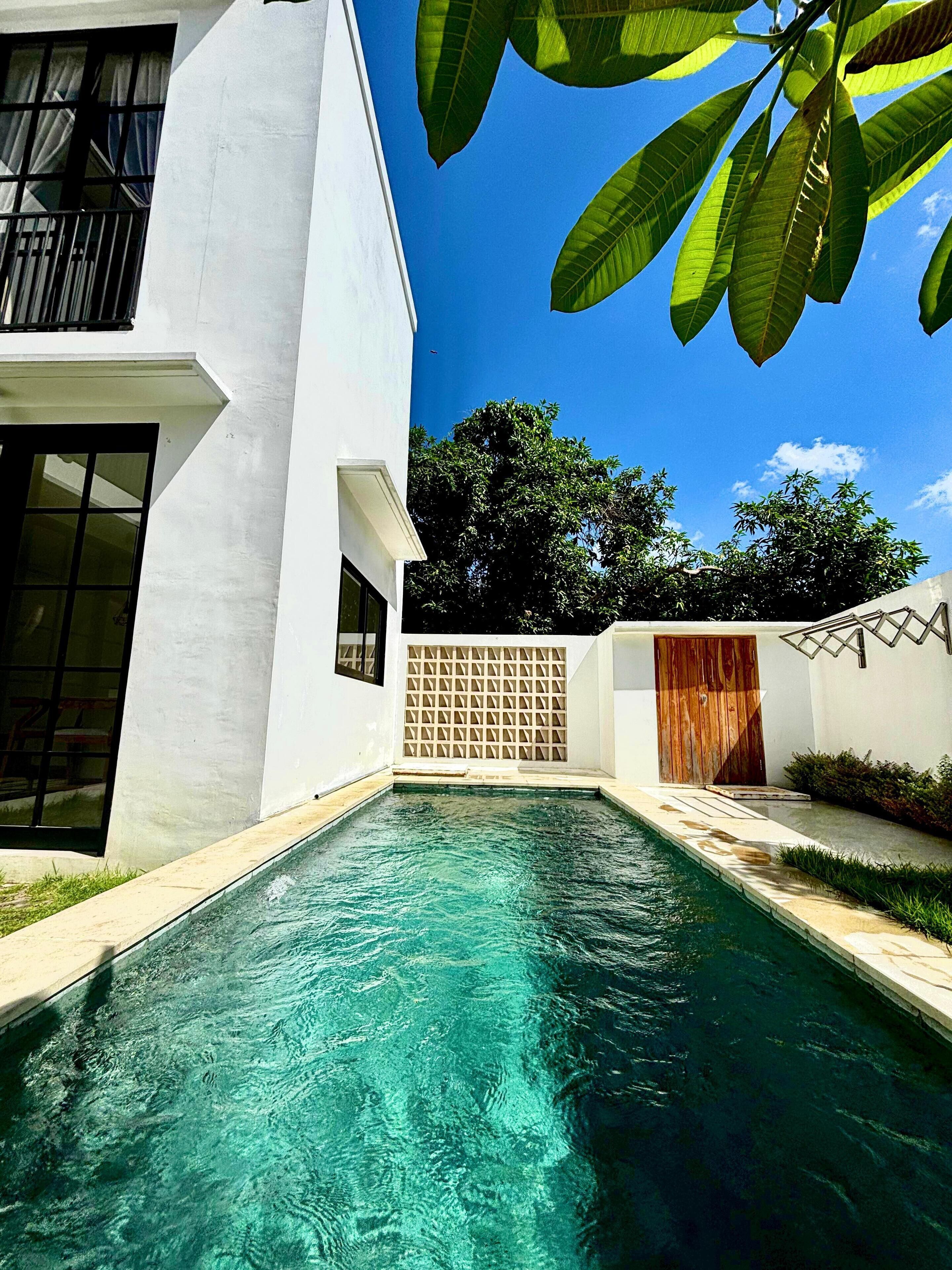A modern house with a swimming pool, a wooden door, and a white exterior.