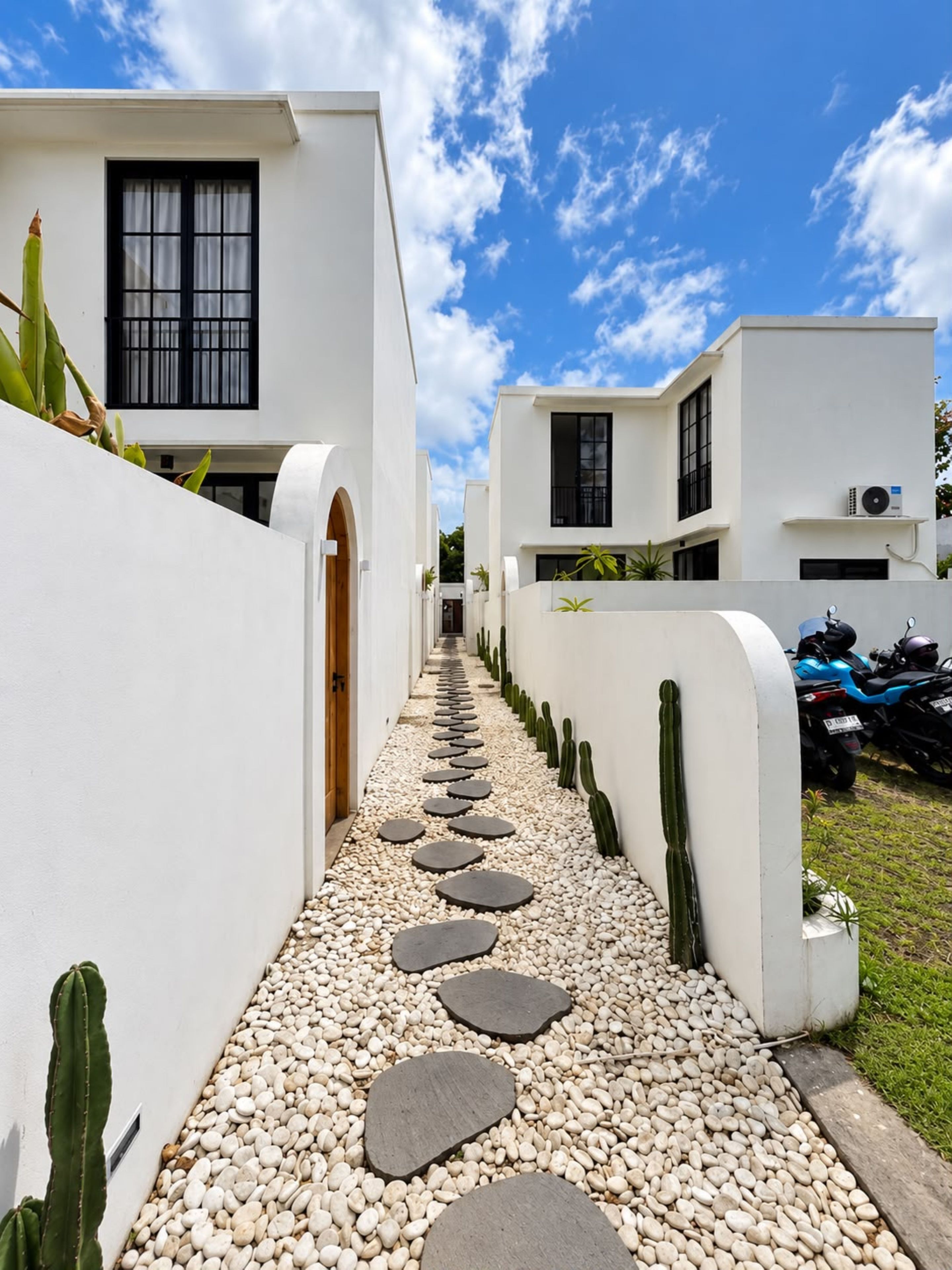 A pathway with stepping stones leading to a white building with a window and a door.