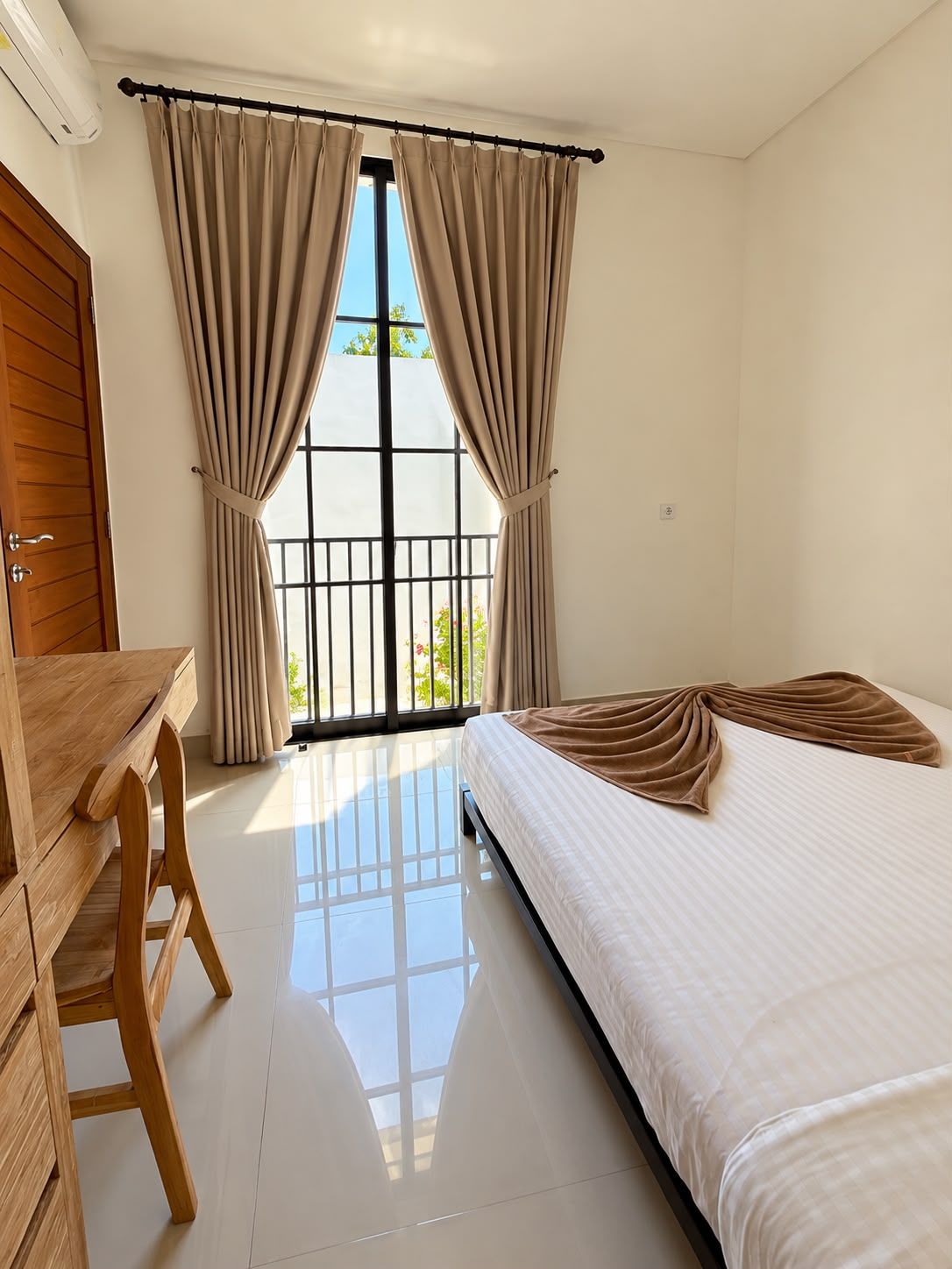 A bedroom with a bed, a wooden desk, and a window with curtains.