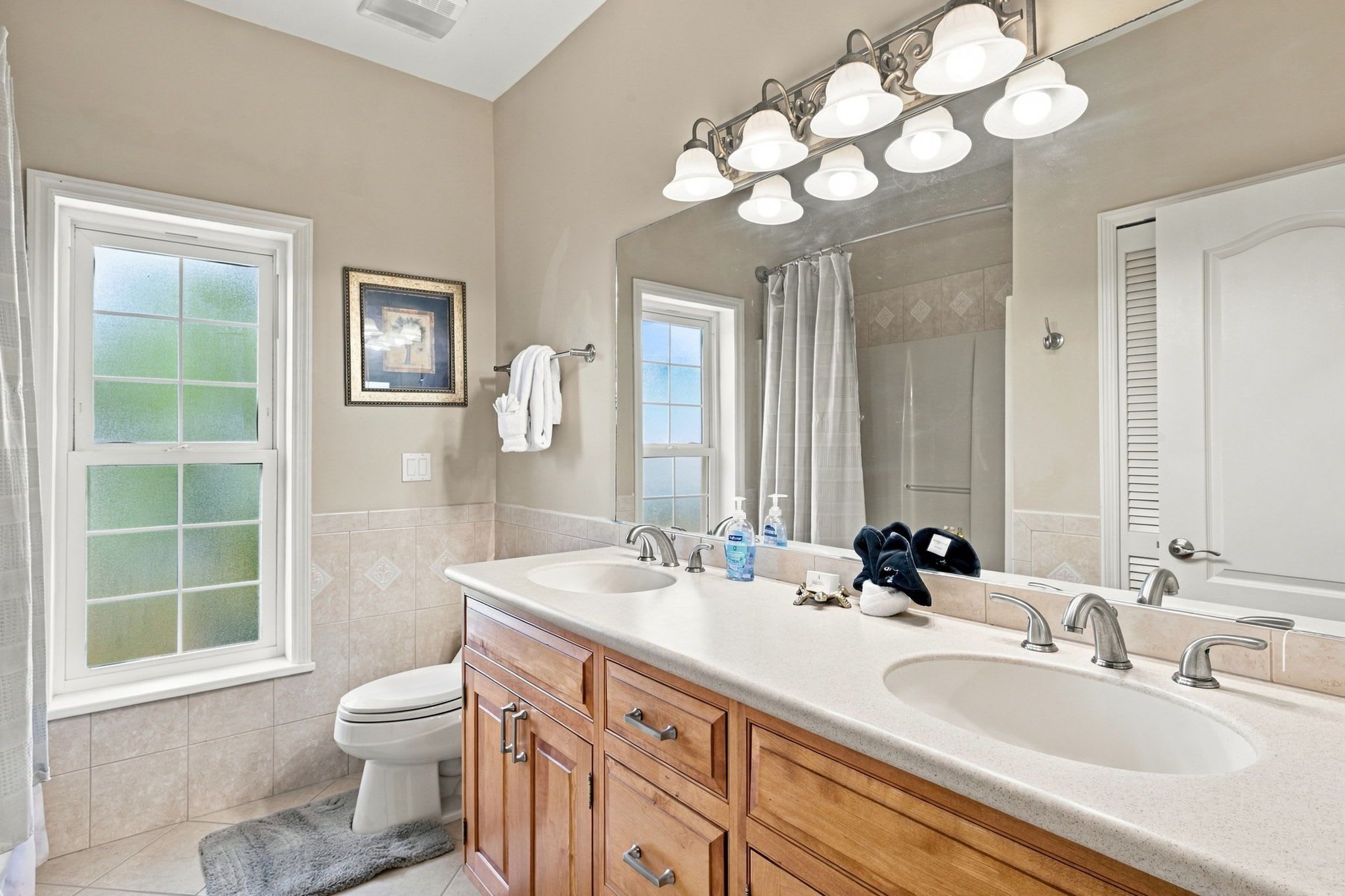 A bathroom with two sinks, a toilet, a shower, and a large mirror with lights.