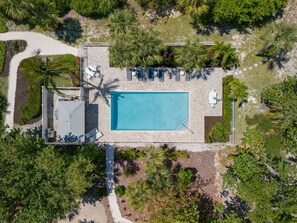 An aerial view of a resort with a central swimming pool, lounge area with sunbeds, and surrounding tropical vegetation.