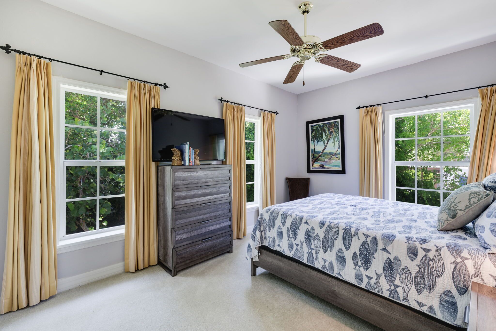 A bedroom with a bed, a dresser, a ceiling fan, and large windows with curtains.