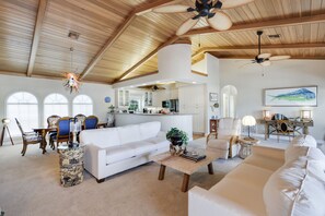 A spacious living area with a high ceiling, a dining area with a table and chairs, a kitchen with white cabinets, and a large window. - Exclusive Sanibel Marina Residence with Pool (Sanibel)