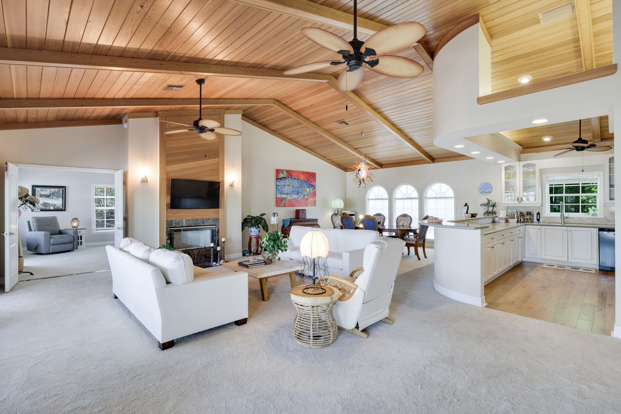 A spacious living area with a fireplace, white furniture, and a kitchen with white cabinets.