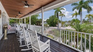 A covered porch with white rocking chairs, ceiling fans, and a view of palm trees and houses. - Exclusive Sanibel Marina Residence with Pool (Sanibel)