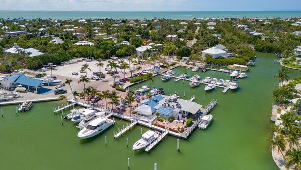 An aerial view of a marina with boats docked, surrounded by lush greenery and residential buildings. - Exclusive Sanibel Marina Residence with Pool (Sanibel)