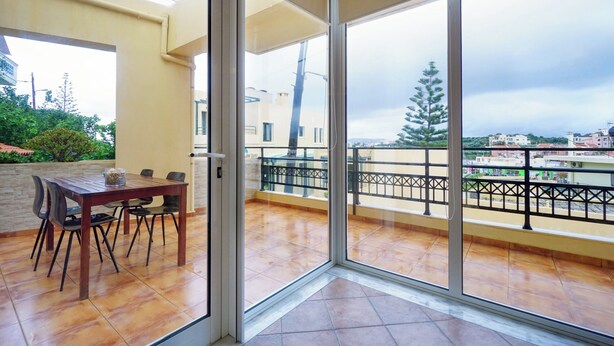 Ein Balkon mit Esstisch und Stühlen, einer Glastür und Blick auf die Stadtlandschaft.