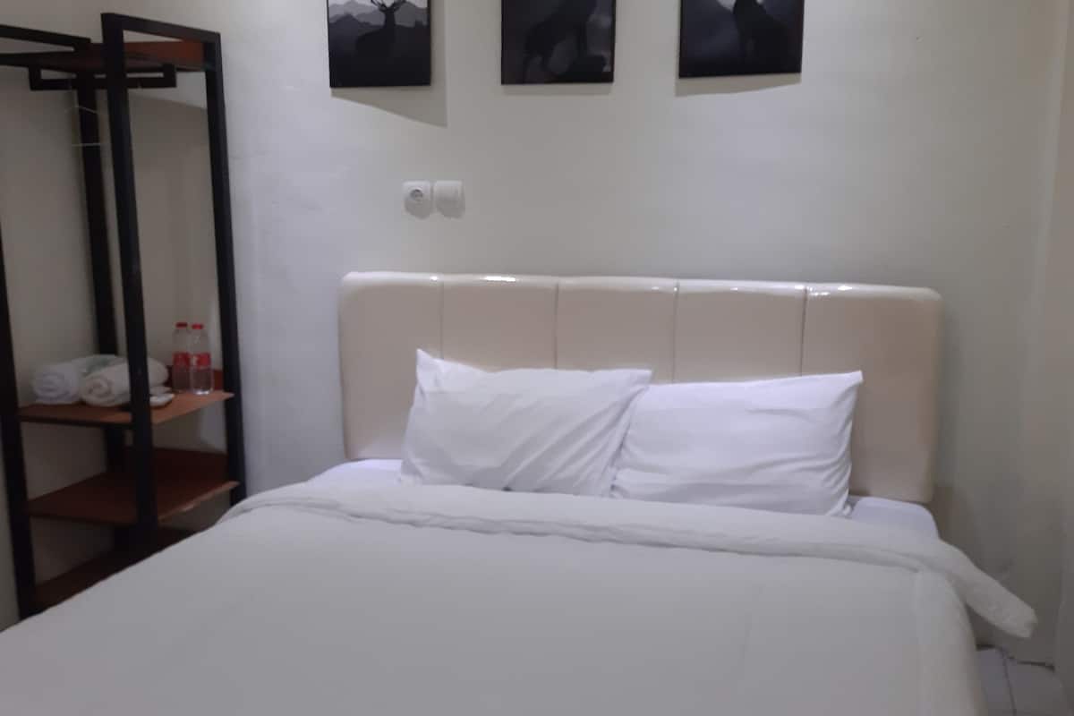 A hotel room with a bed, a wooden shelf with towels and toiletries, and three framed pictures on the wall.