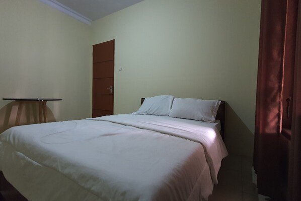 A single bed with white bedding in a room with a closed door and a curtain on the right.