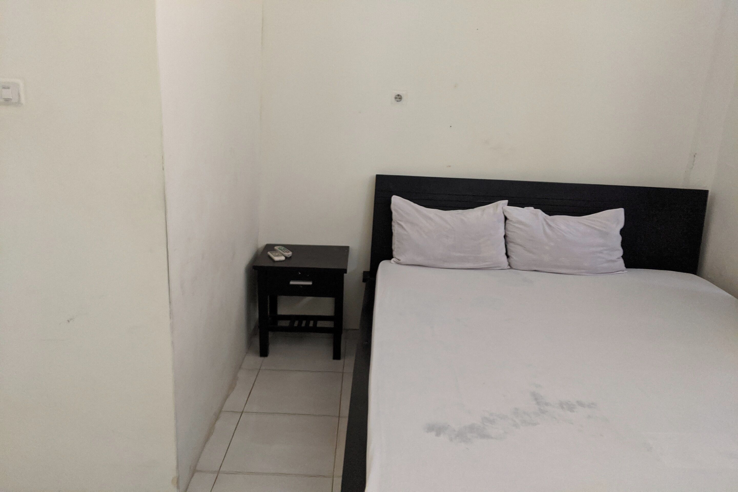A small, simple room with a bed, a nightstand, and a wall socket.
