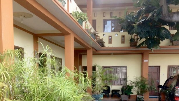 Un immeuble à plusieurs étages doté de balcons, de plantes en pot et d’une voiture garée à l’extérieur.