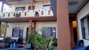 Un bâtiment à deux étages doté d’un balcon, de plantes en pot et d’un petit espace extérieur aménagé pour s’asseoir.