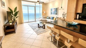 Een moderne woonkamer met een bank, salontafel en een glazen eettafel. Er is een balkon met uitzicht op de oceaan.