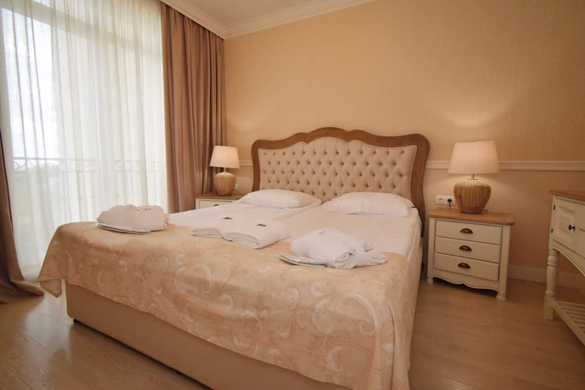 A hotel room with a large bed, two bedside tables, and a window with curtains.
