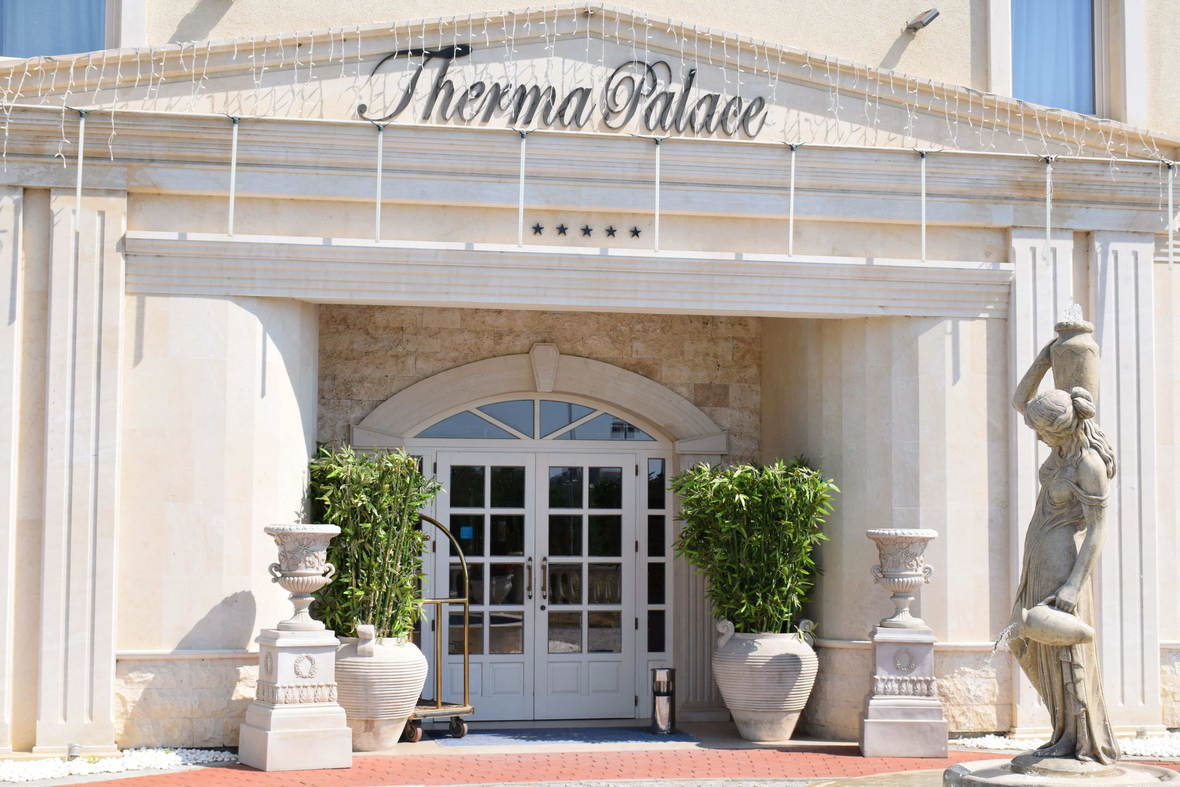 The entrance to Therma Palace with a double door, two potted plants, and a statue.
