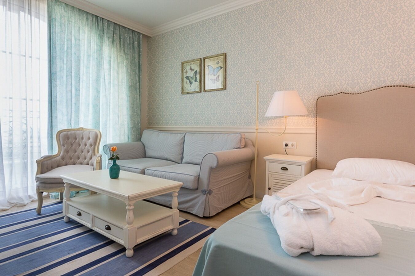 Habitación de hotel con cama, sofá, sillón, una mesita y una mesita de noche.