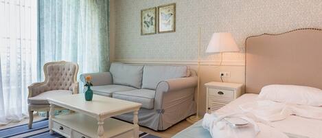Habitación de hotel con cama, sofá, sillón, una mesita y una mesita de noche.