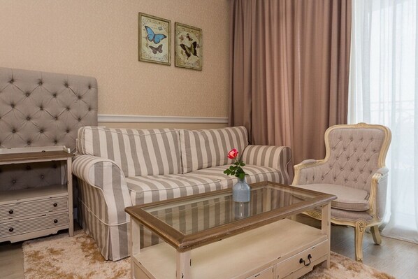 A living room with a striped sofa, a tufted armchair, a glass coffee table with a vase of flowers, and a sideboard. - Therma Palace - Hotel & SPA (Kranevo)