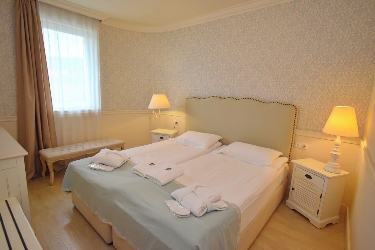 A hotel room with two beds, a bench, a bedside table with a lamp, and a dresser.