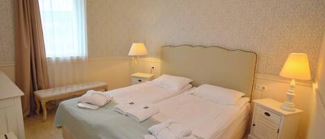 A hotel room with two beds, a bench, a bedside table with a lamp, and a dresser.