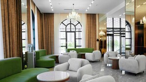 Un salón moderno con sofás verdes, sillones blancos y mesas redondas.