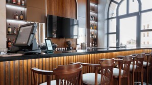 Zona de bar con sillas de madera, mostrador con caja registradora y estantes con botellas.