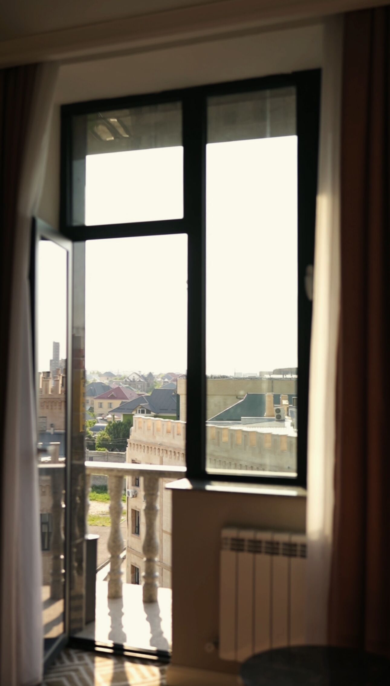 A room with a large window, a radiator, and a view of buildings outside.