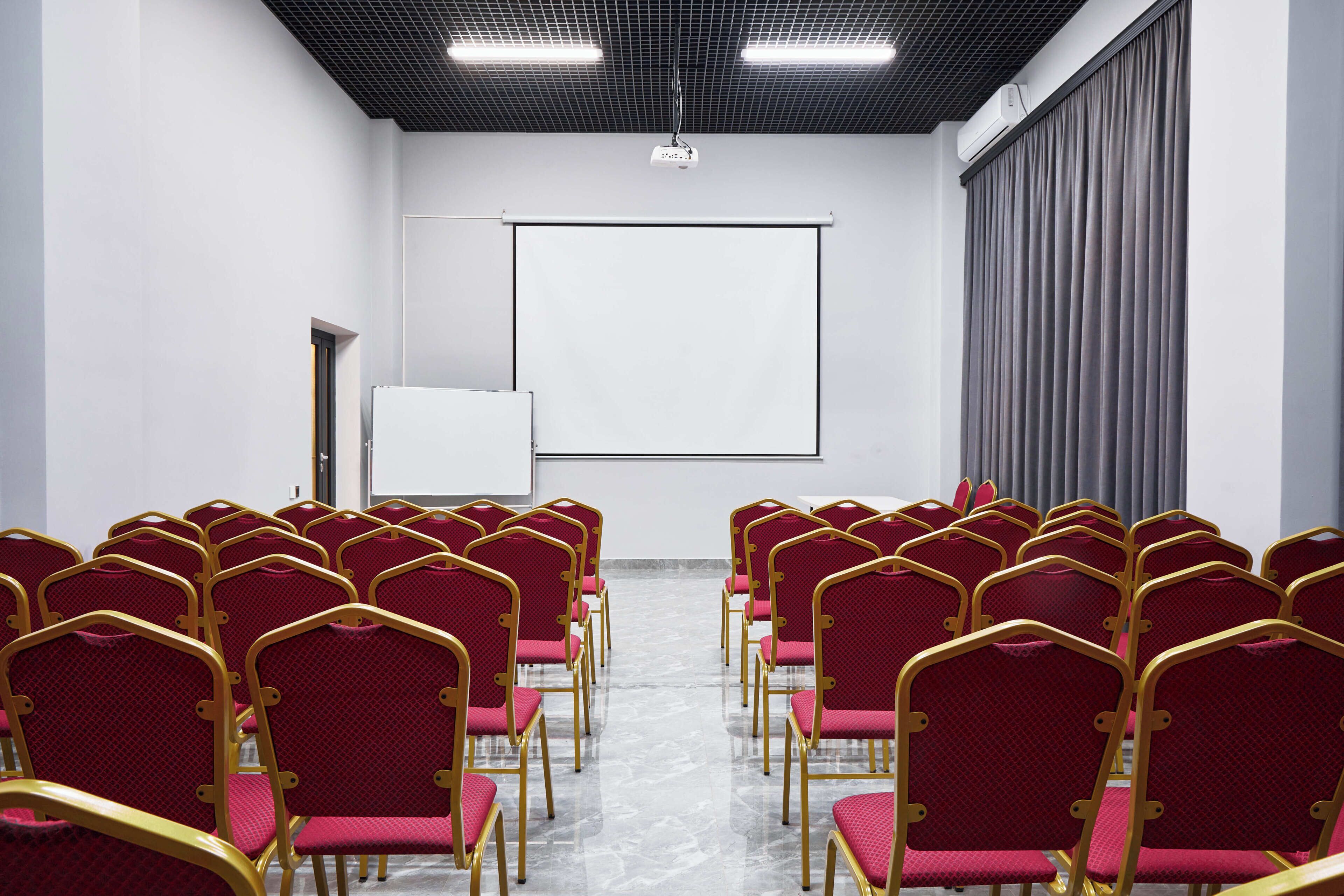 A conference room with rows of red chairs, a whiteboard, and a projector.