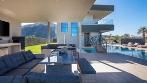Un espace de vie extérieur moderne, doté d’une piscine, de coins salon et offrant une vue sur les montagnes.