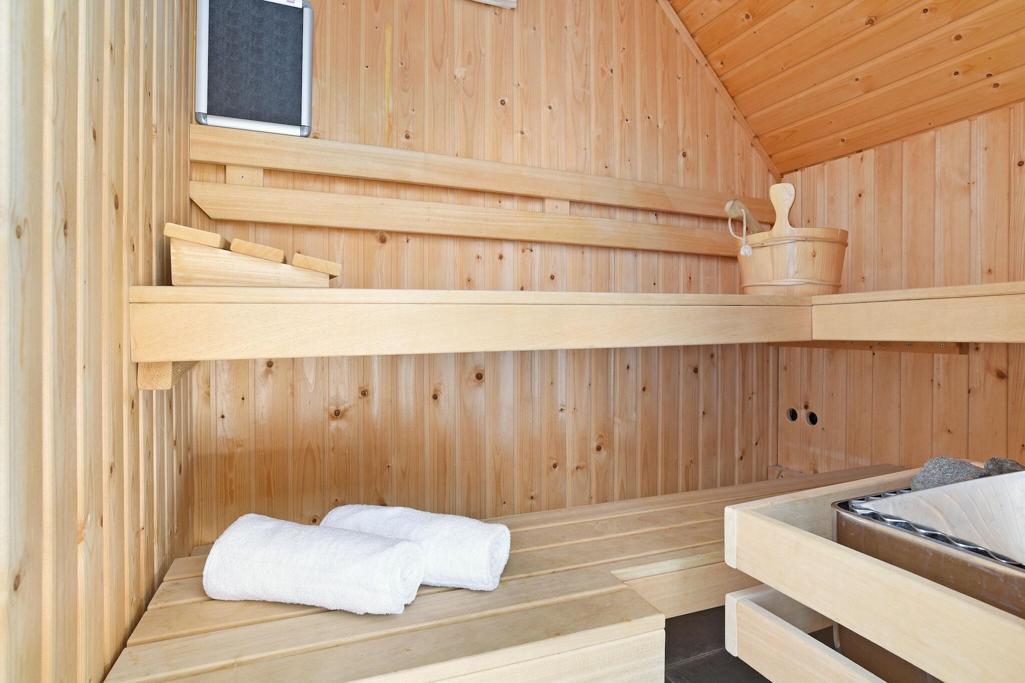 A wooden sauna with a bench, a small window, and a bucket.
