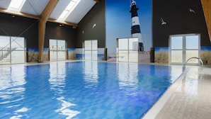 An indoor swimming pool with a mural of a lighthouse, wooden beams, and large windows. - Resort Villa Steps to Sand (Nieuwvliet)