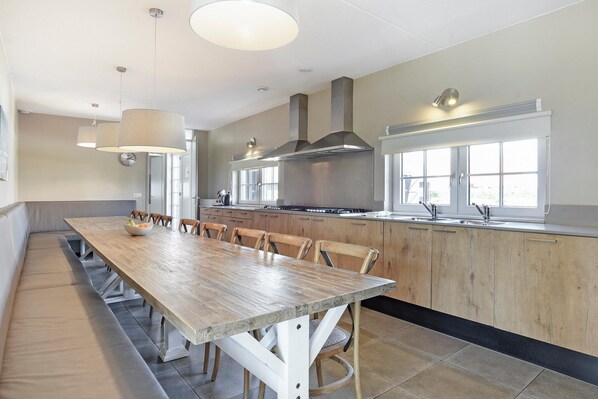 A modern kitchen with a long dining table, wooden cabinets, and a large window.