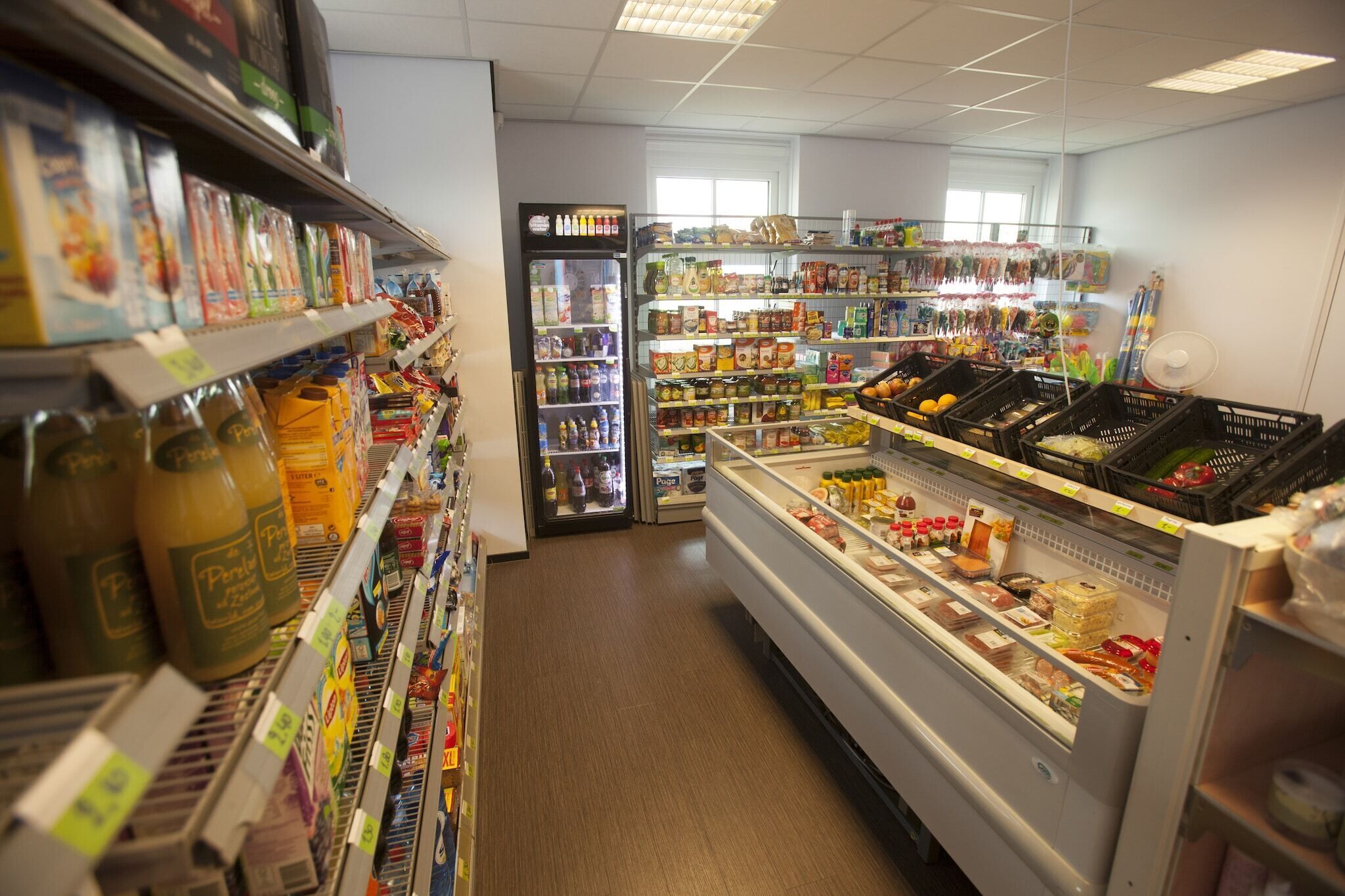 Ein Gang in einem Supermarkt mit Regalen voller verschiedener Produkte, Kühlregalen und einer Auslage mit Feinkostprodukten.