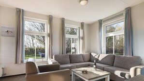 A modern living room with a sectional sofa, a coffee table, and large windows with curtains. - Beach Retreat w/ Garden (Nieuwvliet)