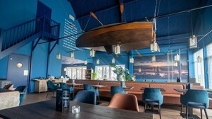 A modern interior with a wooden table, blue chairs, and a seating area with orange sofas. - Beach Retreat w/ Garden (Nieuwvliet)