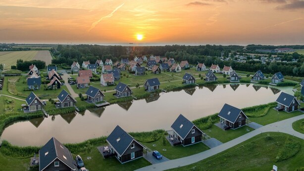Un quartier résidentiel où les maisons sont disposées autour d’un étang central, sous un ciel embrasé par le coucher du soleil.