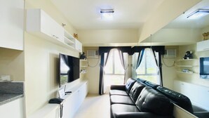Un saló modern amb un sofà de cuir negre, un televisor de pantalla plana muntat sobre un moble blanc i un mirall gran a la paret.