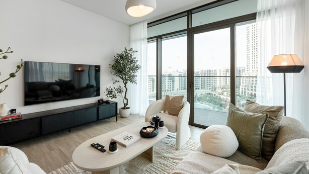 Ein modernes Wohnzimmer mit Flachbildfernseher, Couchtisch, Sofa, Topfpflanze und einem großen Fenster mit Blick auf die Stadt.