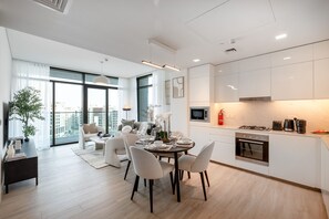 Eine moderne Küche mit weißen Schränken, ein Essbereich mit rundem Tisch und Blick auf die Stadt durch große Fenster.
