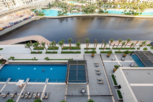 A rooftop pool area with multiple swimming pools, palm trees, and lounge chairs.