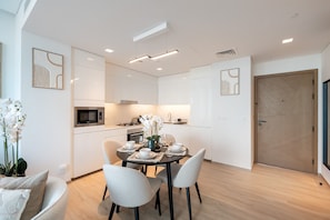 A modern kitchen with white cabinetry, a dining table set for four, and a microwave.