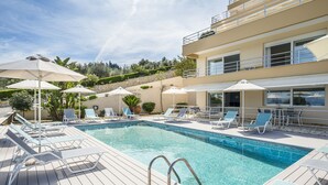 Ein Poolbereich mit Liegestühlen und Sonnenschirmen, umgeben von einer Steinmauer und Pflanzen.