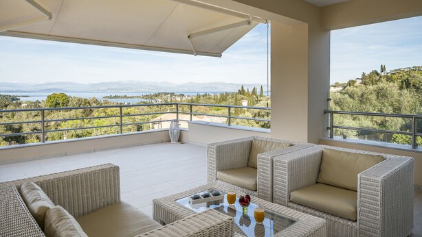 Ein Balkon mit Korbmöbeln, einem Glastisch und Blick auf einen See und Berge.