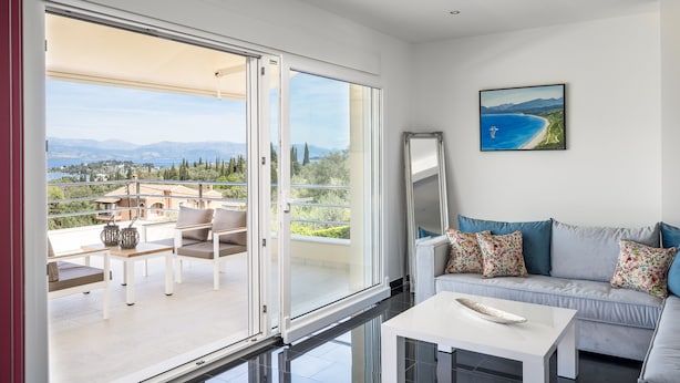 A modern living room with a balcony, a sofa with patterned cushions, a white coffee table, and a painting of a coastal landscape.