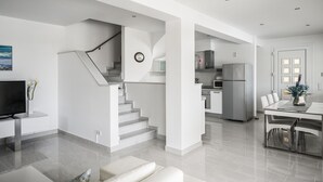 Ein modernes Interieur mit einer Treppe zum zweiten Stock, einer Küche mit Edelstahlgeräten und einem Essbereich mit einem Glastisch.
