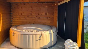 Un jacuzzi en una cabaña de madera con una puerta negra y un par de pantuflas en el suelo.