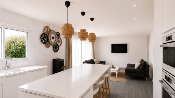 Una cocina moderna con una isla central, taburetes de bar, una zona de comedor con sofá y un televisor montado en la pared.