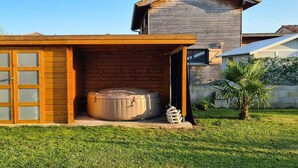 Una estructura de madera con puerta de vidrio, un jacuzzi y una pequeña palmera en el patio.