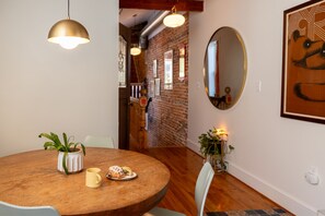 A dining area with a round wooden table, a potted plant, and a plate of food. - Wyatt's Saloon Guest House 2 (Baltimore)