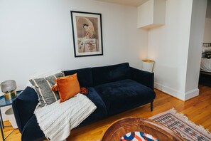 A dark blue sofa with multiple cushions, a framed picture on the wall, a lamp, and a wooden coffee table with a colorful rug. - Wyatt's Saloon Guest House 2 (Baltimore)